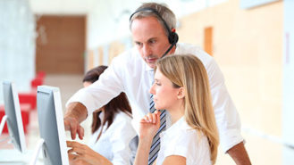 Man with headset discussing screen item with seated woman
